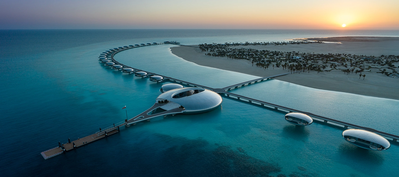Aerial view of Shebara Resort at sunset, featuring a crescent of mirrored overwater villas and a central circular building.
